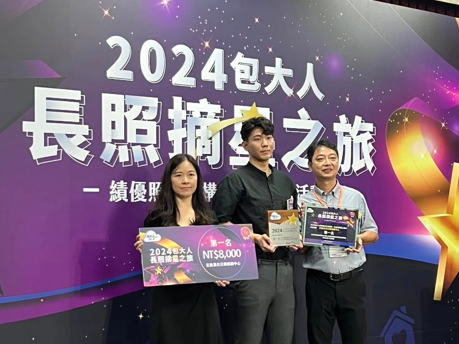 2024 包大人長照摘星之旅頒獎現場，三人於印有活動主視覺的背板前合影，手持第一名獎牌與獎座。